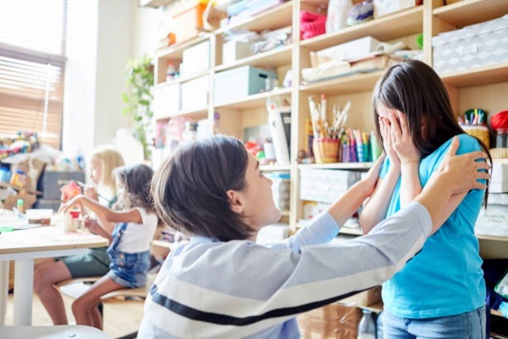 Teacher comforting anxious child in bright, welcoming classroom setting