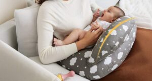 New mom smiling while breastfeeding baby on gray Momcozy Original nursing pillow with perfect arm and neck support