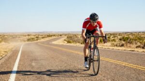 Cyclist riding a road bike on a sunlit highway during a hot Texas afternoon.